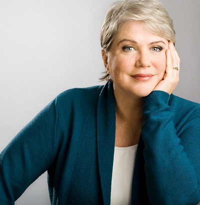 Julia Sweeney, wearing a turquoise jacket, leans her face on her left hand.
