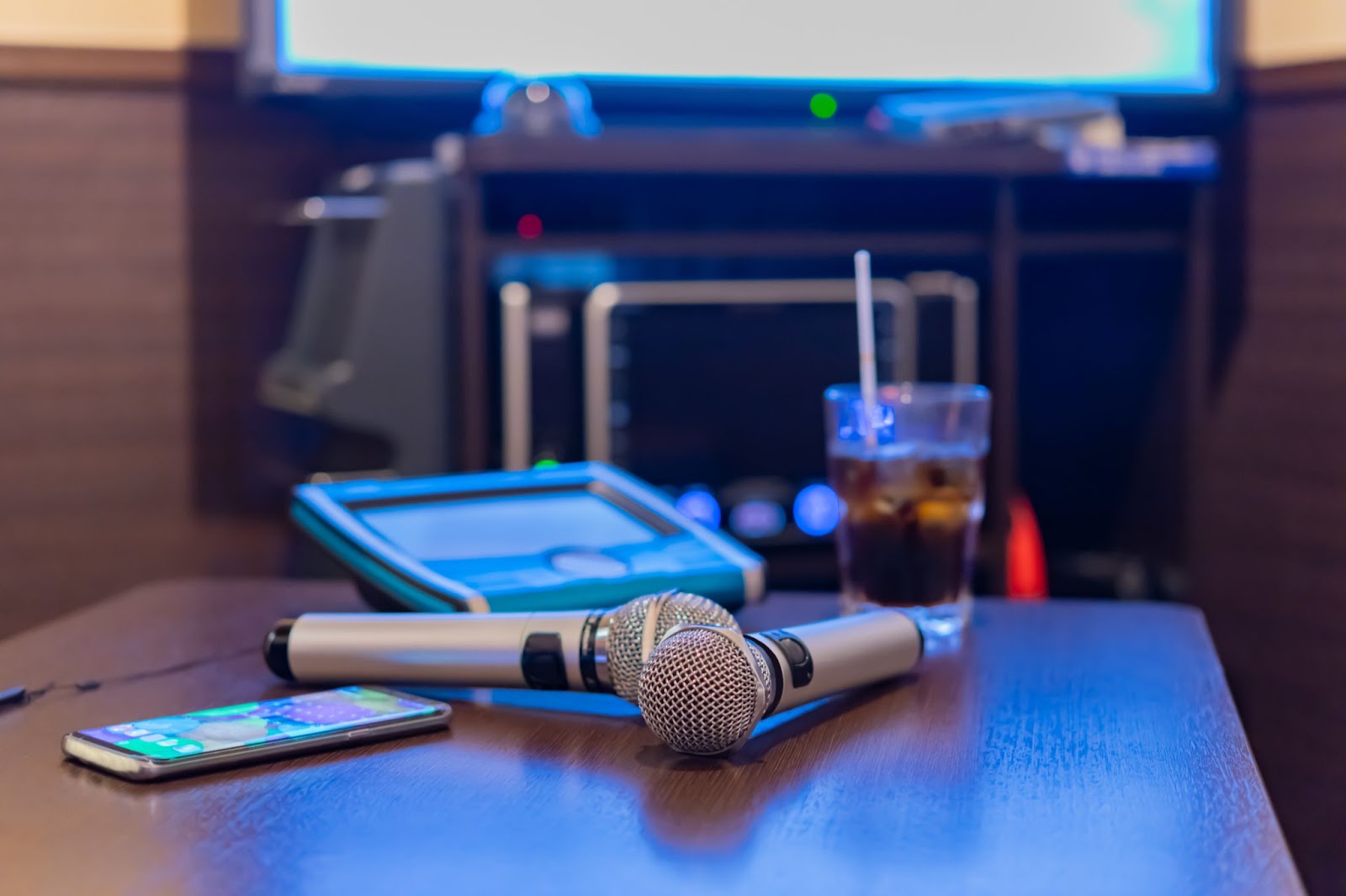 Two microphones on a table next to a cell phone, a drink, and a karaoke machine.