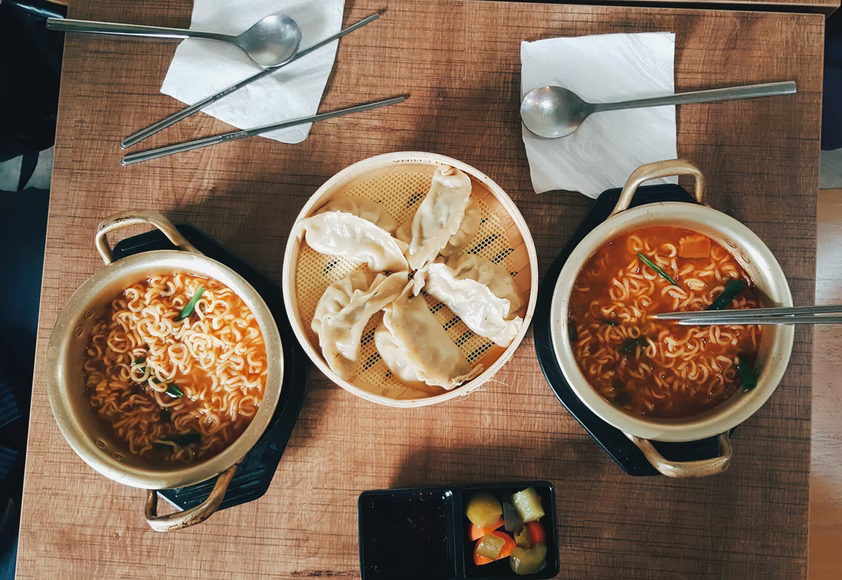 Two pots with Korean noodles and a single container with dumplings.