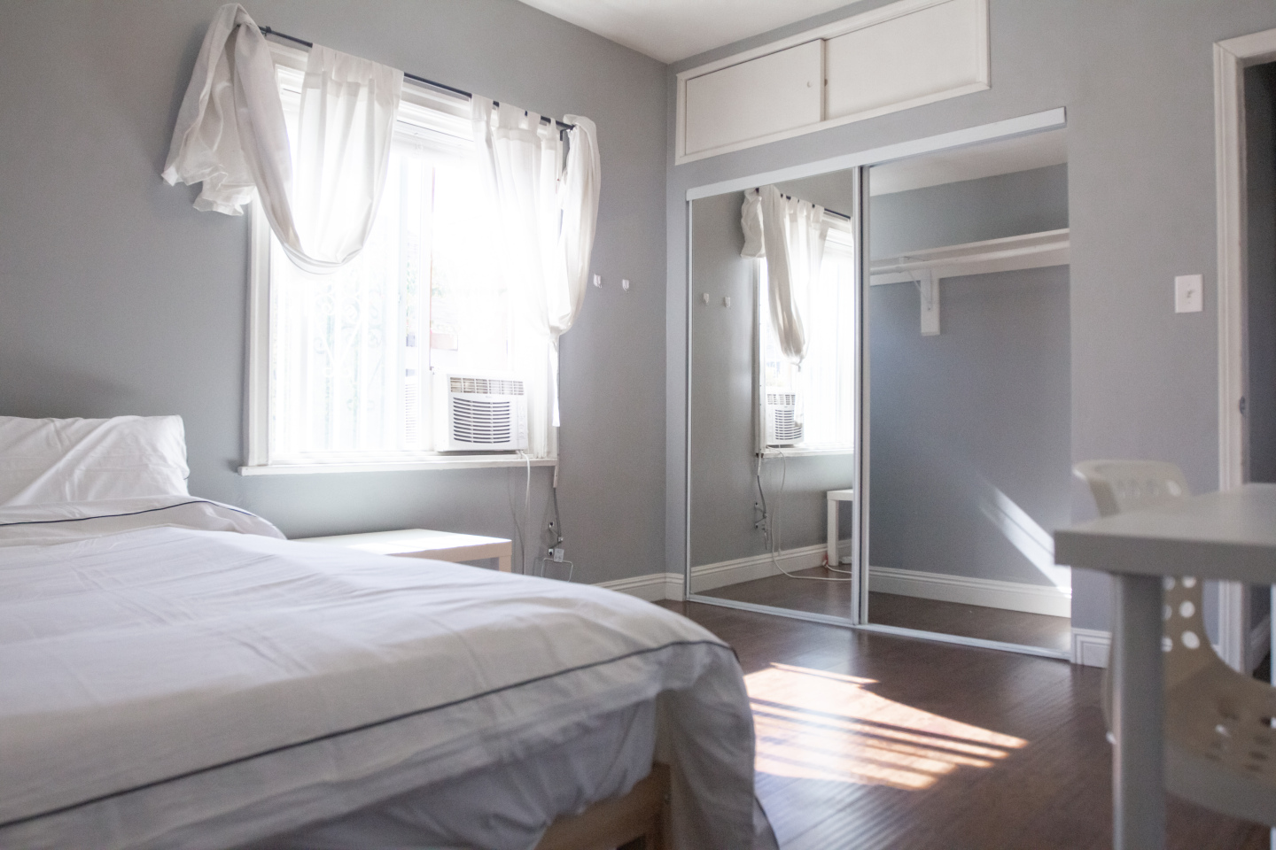 Hardwood floors, white curtain , gray comforter on bed 