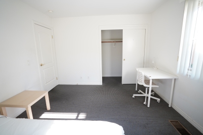 white bedroom, grey carpet, small light brown table, white computer desk with white rolling chair 