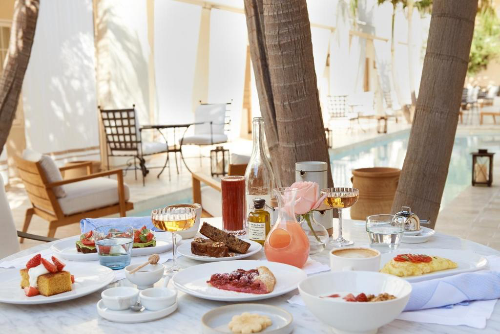 A table filled with various breakfast and dessert dishes outside next to a pool.