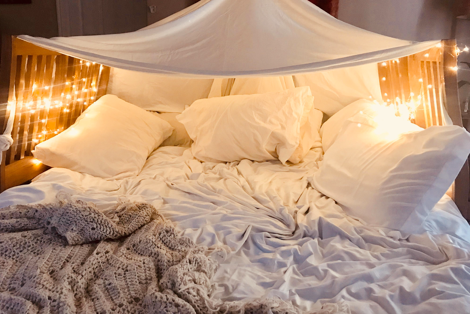 comfy white bed surround by fairy lights 
