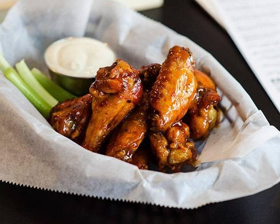 Buffalo wings in a basket lined with greaseproof paper, dipping sauce, and julienned cucumber.