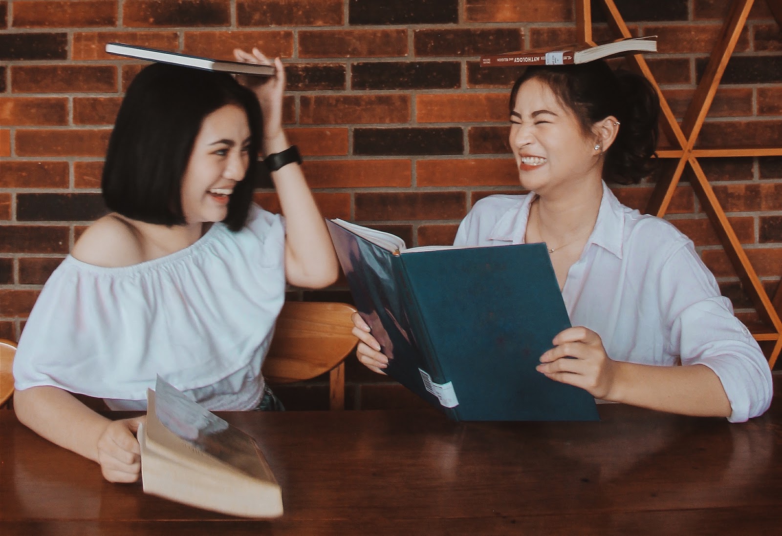 two women laughing with books on their head