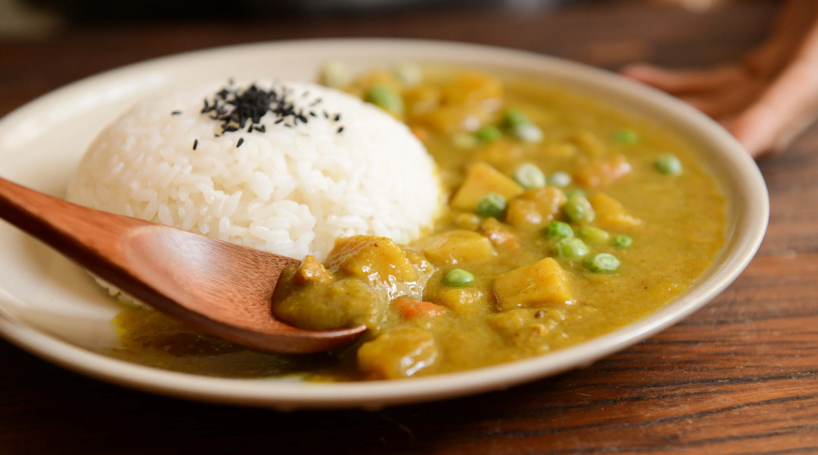  A plate of vegetable curry with a serving of rice and a wooden spoon.
