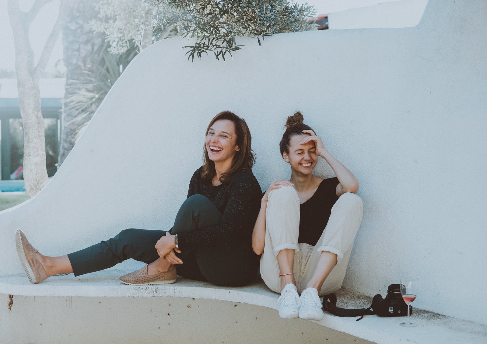 two girls laughing and sitting on the ground against white background 