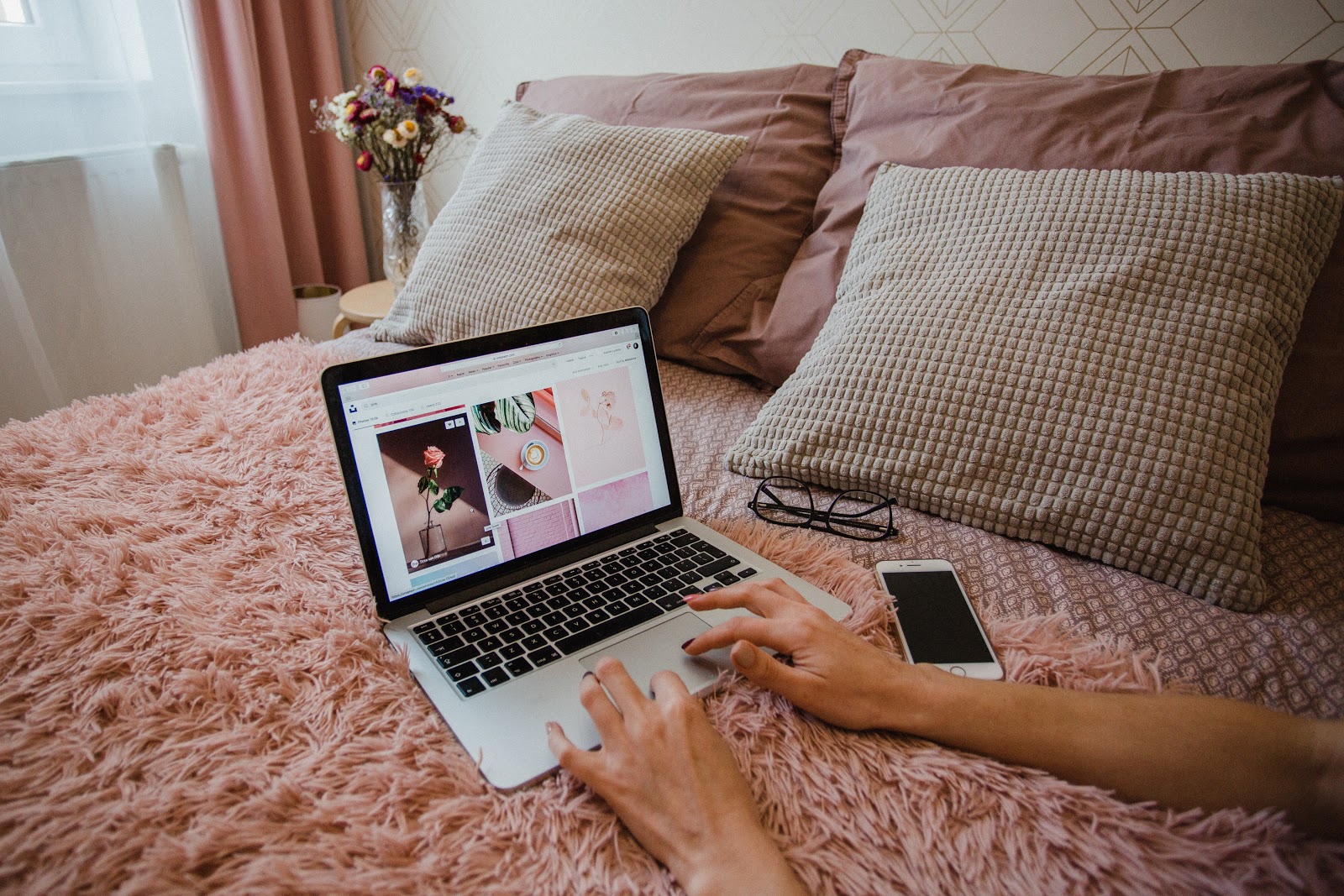 someone typing on MacBook on bedside with pink flurry blanket
