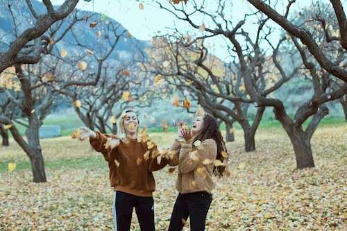 Two laughing people playing with fall leaves in the woods.